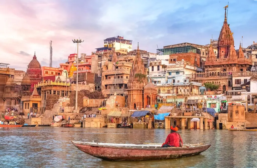 Vista del río Ganges en Varanasi, India, con una persona en un bote y los templos y edificios históricos en la orilla.