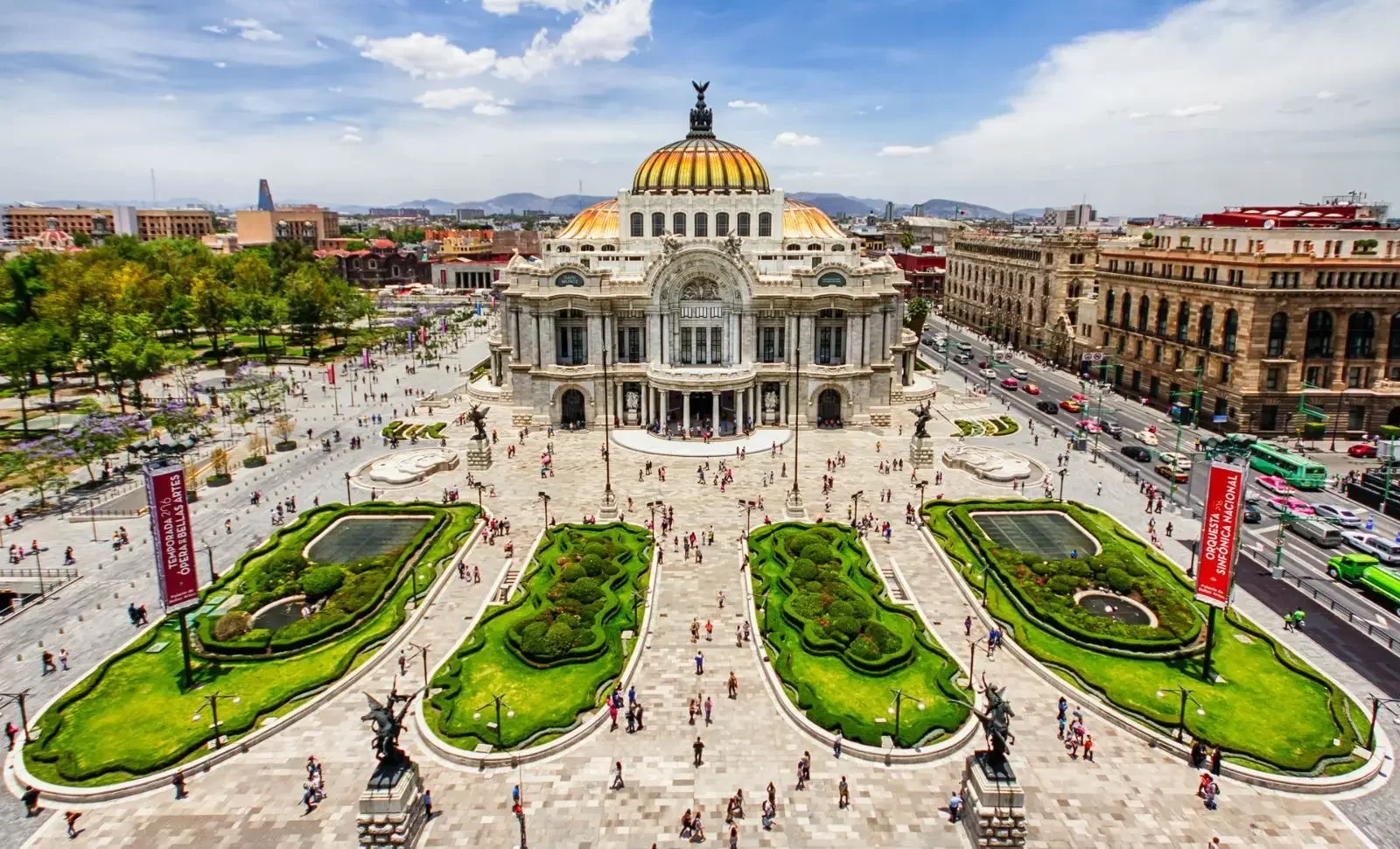 Vista aérea del Palacio de Bellas Artes en la Ciudad de México, rodeado de jardines y visitantes bajo un cielo despejado.