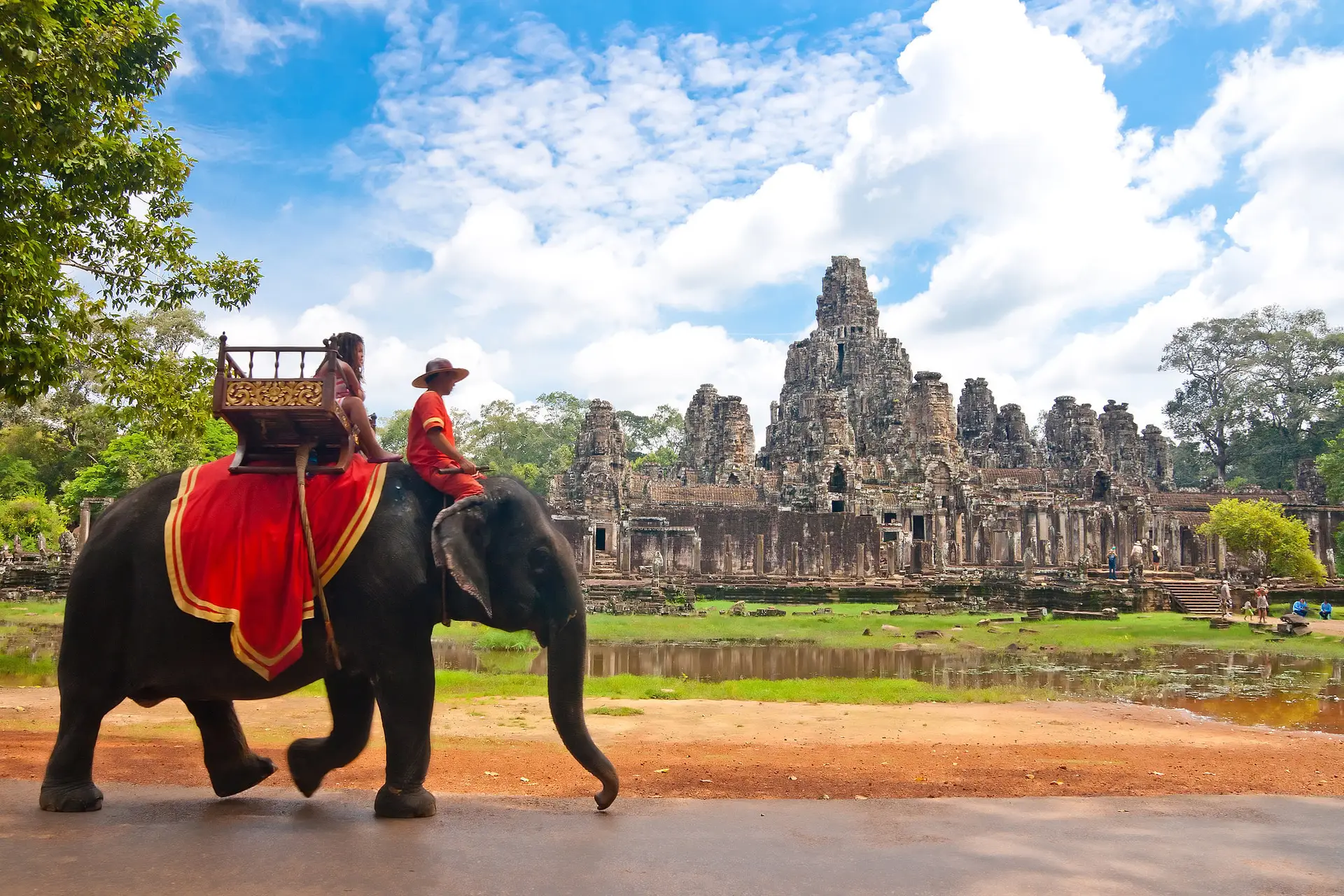 Fotografía en blanco y negro de un templo en Angkor, Camboya, con un elefante y su jinete en primer plano, y ruinas antiguas en el fondo.