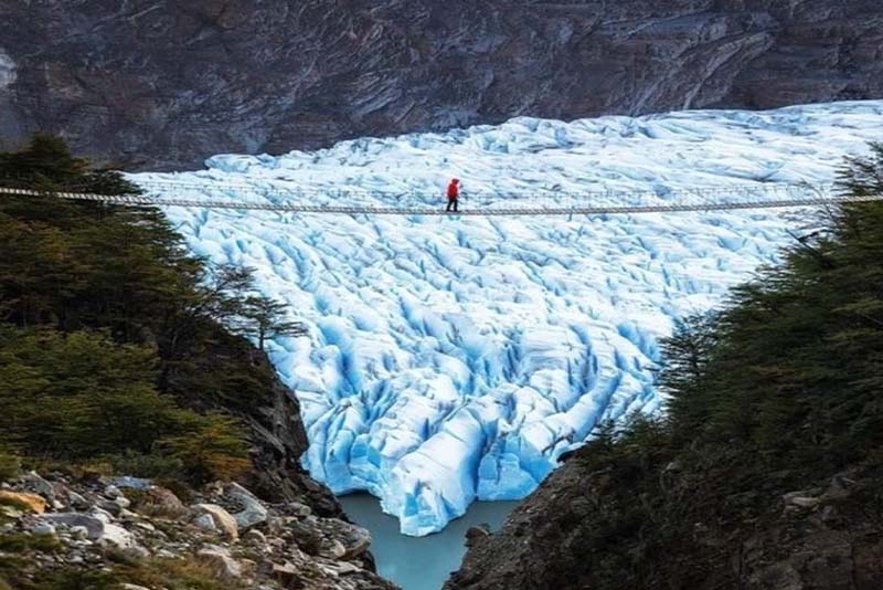 Imagen señor andandotela por un puente por encima de glaciar.